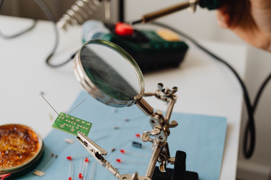 Detailed view of a magnifying glass examining a small circuit board with soldering tools nearby.